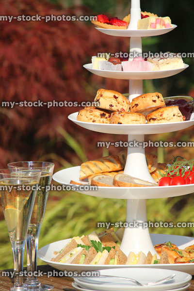 Stock image of afternoon tea / cream tea, tiered cake stand, sandwiches, cakes, scones, garden