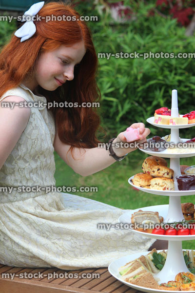 Stock image of afternoon tea / cream tea, cake stand tiers, girl eating cakes scones sandwiches