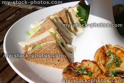Stock image of afternoon tea / cream tea, white tiered cake stand, sandwiches, mini quiches