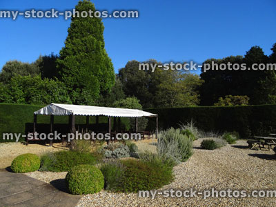 Stock image of round wooden picnic tables, ornamental gravel garden / park, awning shading