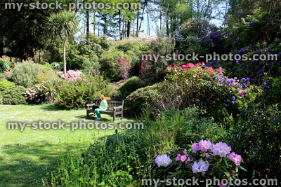 Stock image of girl sat on wooden bench by rockery (rock garden) flowers