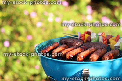 Stock image of kettle charcoal barbecue BBQ in garden, sausages, burgers, kebabs
