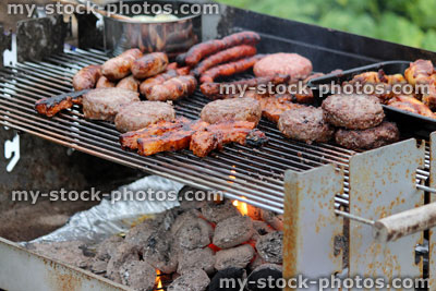 Stock image of charcoal barbecue, garden trolley BBQ grill, sausages, burgers, chicken drumsticks, saucepan