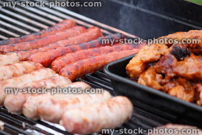 Stock image of charcoal barbecue, garden trolley BBQ grill, sausages, chicken drumsticks