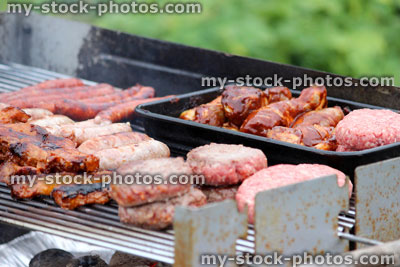 Stock image of charcoal barbecue, garden trolley BBQ grill, sausages, burgers, chicken legs