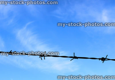 Stock image of barbed wire against blue sky with clouds