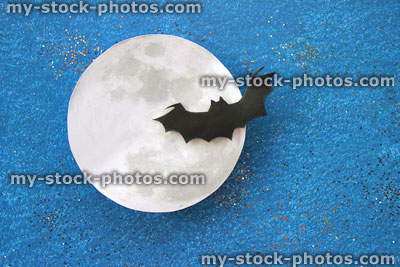 Stock image of black bat silhouette flying in front paper moon, Halloween village / Halloween background