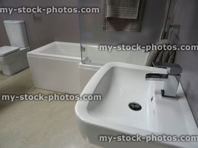 Stock image of modern bathroom suite, white L shaped shower bath, glass shower screen, wall hung basin sink