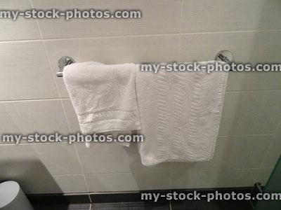 Stock image of bathroom tiles, fluffy white towels hanging on chrome towel rail