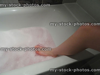 Stock image of modern white bathroom, naked woman getting into bath / bubblebath / bubbles