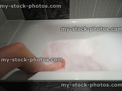 Stock image of modern white bathroom, naked woman getting into bath / bubblebath / bubbles