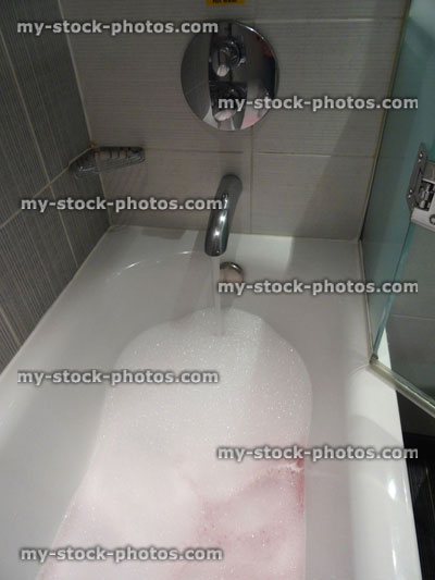 Stock image of modern white bathroom suite / bath, black white tiles, pink bubbles bubblebath