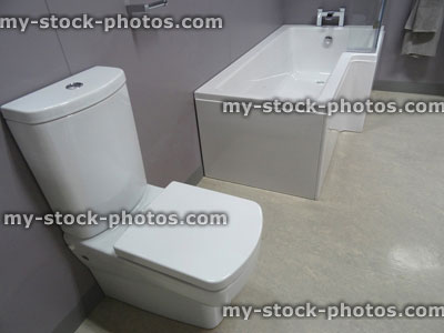 Stock image of modern bathroom suite, white L shaped shower bath, glass shower screen, toilet / WC