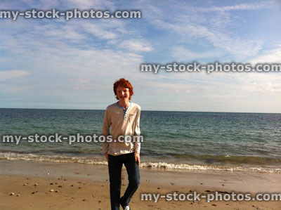 Stock image of boy standing on beach with sun, sea background