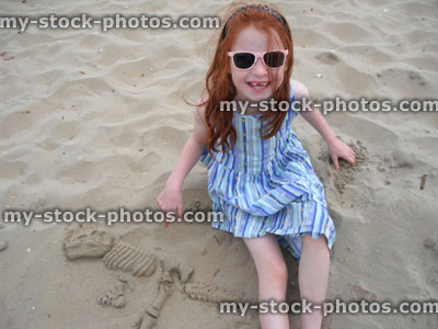 Stock image of little girl on sandy beach with fossil dinosaur casting