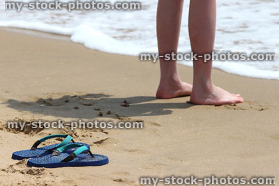 Stock image of girl's legs by sea, barefoot on beach, flip flops, thongs, sand