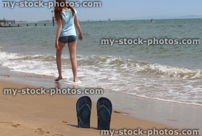 Stock image of girl walking barefoot on beach, flip flops / thongs / sand
