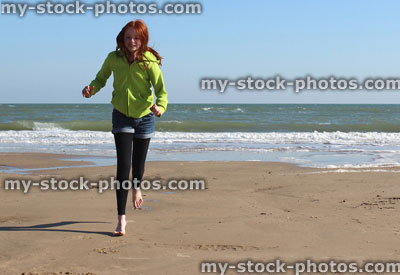 Stock image of girl running along beach with sea in background