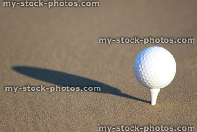 Stock image of golf ball on sandy seaside beach, with tee / shadow