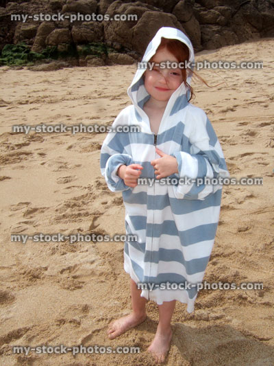 Stock image of little girl wearing dad's oversized hoodie on a sandy beach