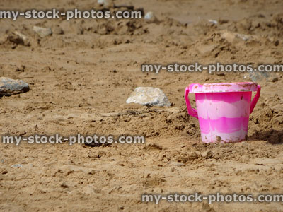 Stock image of pink plastic seaside bucket with handle on beach sand