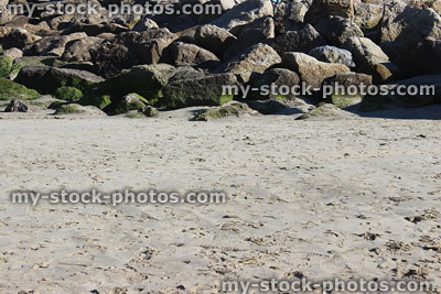 Stock image of pile of rocks on beach sand, rock armour / riprap