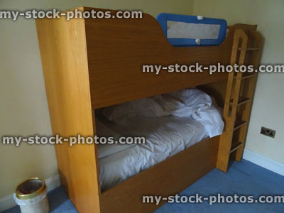 Stock image of wooden bunk bed in bedroom with bed guard rail / bedrail