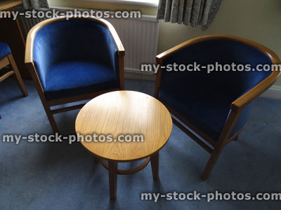 Stock image of two blue cushioned, wooden curved armchairs, banana shape chairs, round table, bucket seats