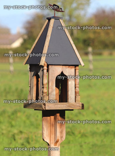 Stock image of ornate wooden bird table, pyramid slate roof, garden background