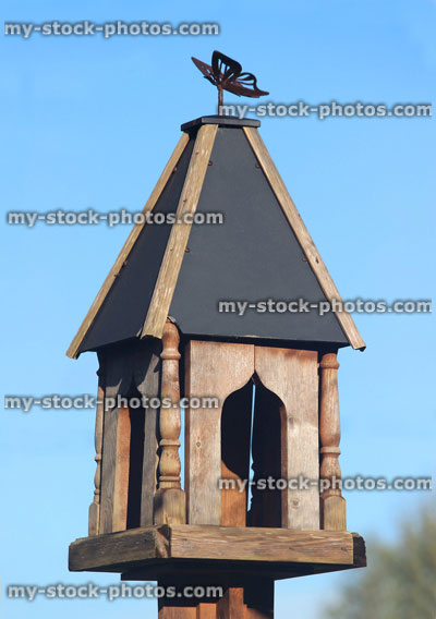 Stock image of ornate wooden bird table, pyramid slate roof, sky background