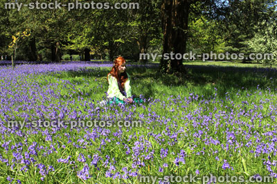 Stock image of girl with long red hair sitting in wildflower bluebell meadow
