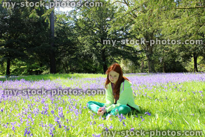 Stock image of girl with red hair sitting in field of bluebell flowers