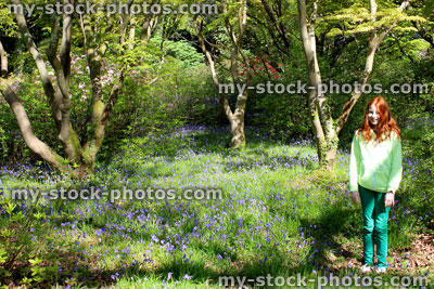 Stock image of girl standing next to Japanese maples and bluebells, woodland garden