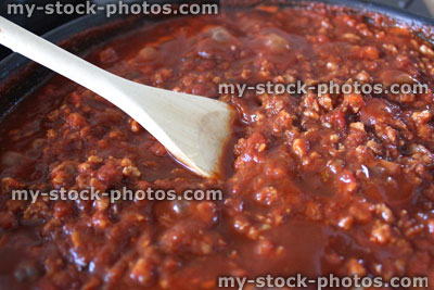 Stock image of Bolognese sauce cooking in frying pan, wooden spoon