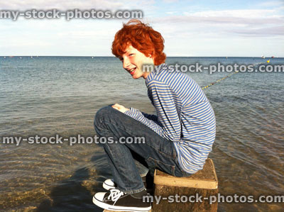 Stock image of red head teenage boy sat upon beach groyne post