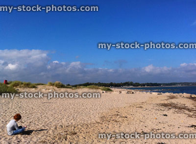 Stock image of boy sat on a remote beach near sand dunes