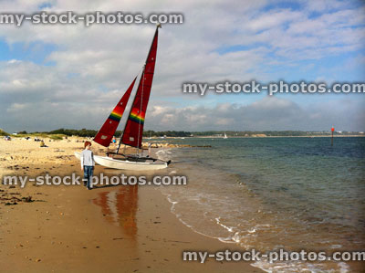 Stock image of red head teenage boy walking past red sailed boat