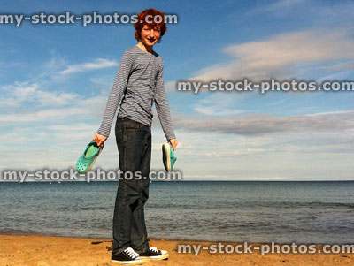 Stock image of red head teenage boy stood on beach with cheeky grin