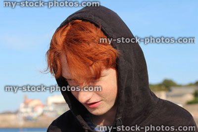 Stock image of red hair teenage boy wearing black hoodie, youth daydreaming at beach