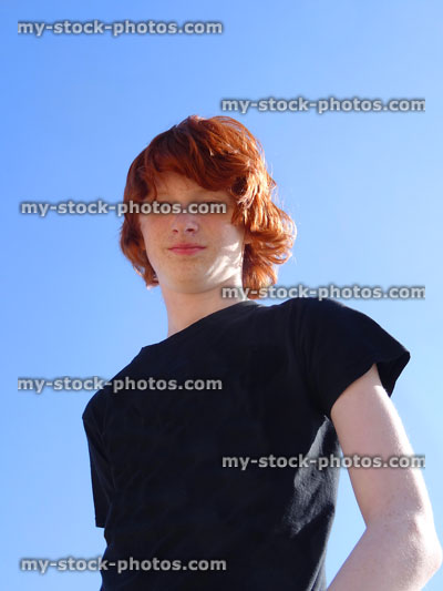 Stock image of teenage boy with red hair, black T shirt, against sky