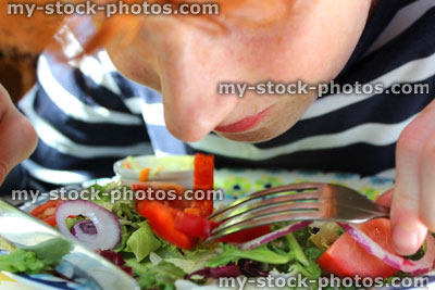 Stock image of boy eating plate of salad, lettuce, tomatoes, peppers, red onion, knife fork