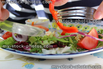 Stock image of boy eating plate of salad, lettuce, tomatoes, peppers, red onion, knife fork