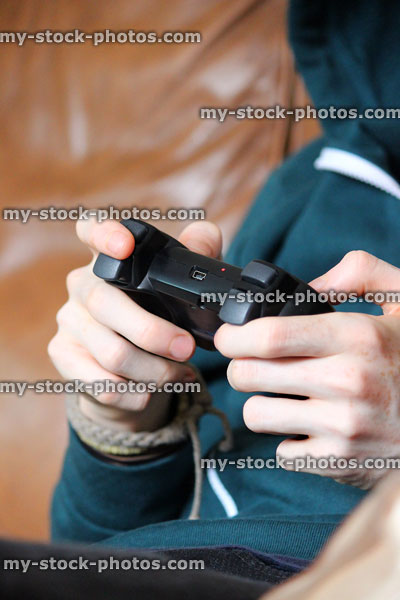 Stock image of hoodie boy playing on television video game, wireless controller