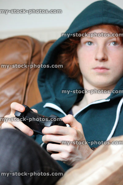 Stock image of teenage boy wearing hoodie, playing on video game controller