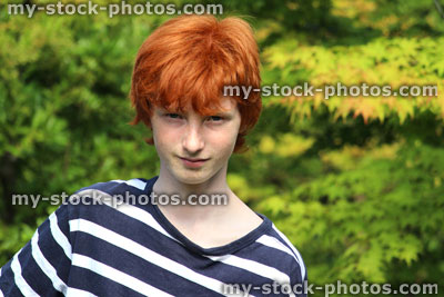 Stock image of teenage boy wearing stripy top, red hair, smiling in garden