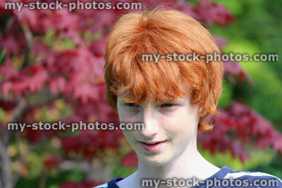 Stock image of teenage boy wearing stripy top, red hair, smiling in garden