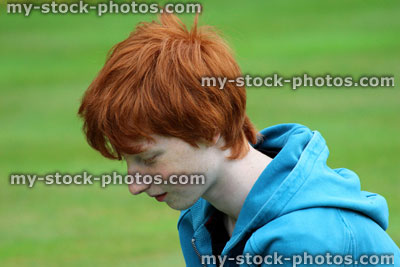 Stock image of young boy with short red hair smiling in garden, looking down