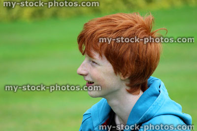 Stock image of young boy with short red hair smiling in garden, looking up