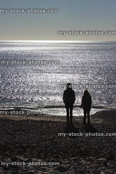 Stock image of boy and girl silhouettes on beach, facing sunshine