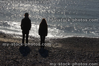 Stock image of boy and girl silhouettes on beach, against sunlight